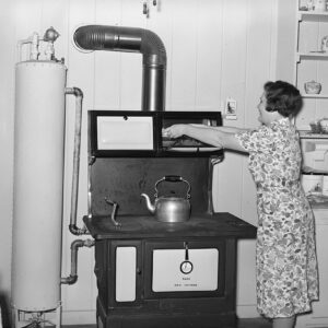 Woman at stove in kitchen putting a dish in an upper compartment