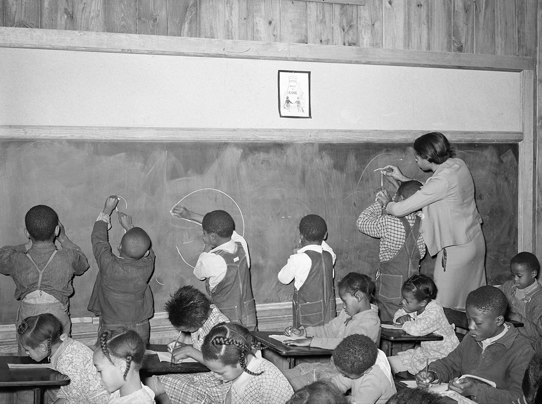 African American children and teacher at blackboard in classroom