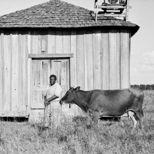 African American woman with cow in front of wooden house
