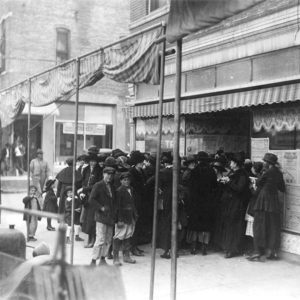 men and women and children in dark clothing and hats standing in front of a store front