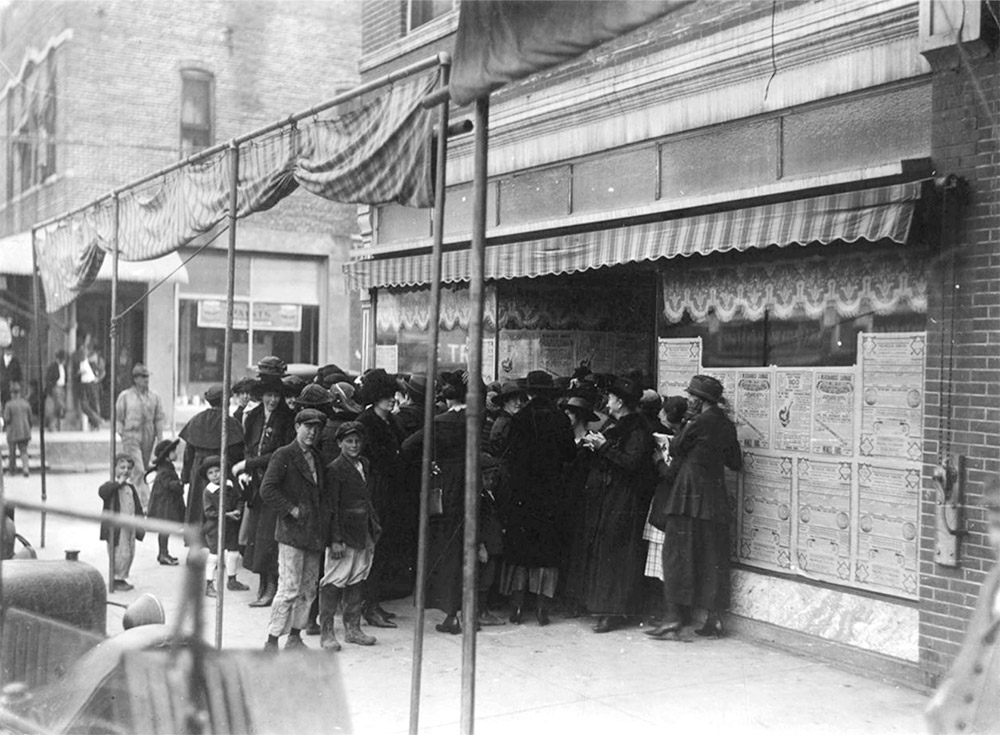 men and women and children in dark clothing and hats standing in front of a store front
