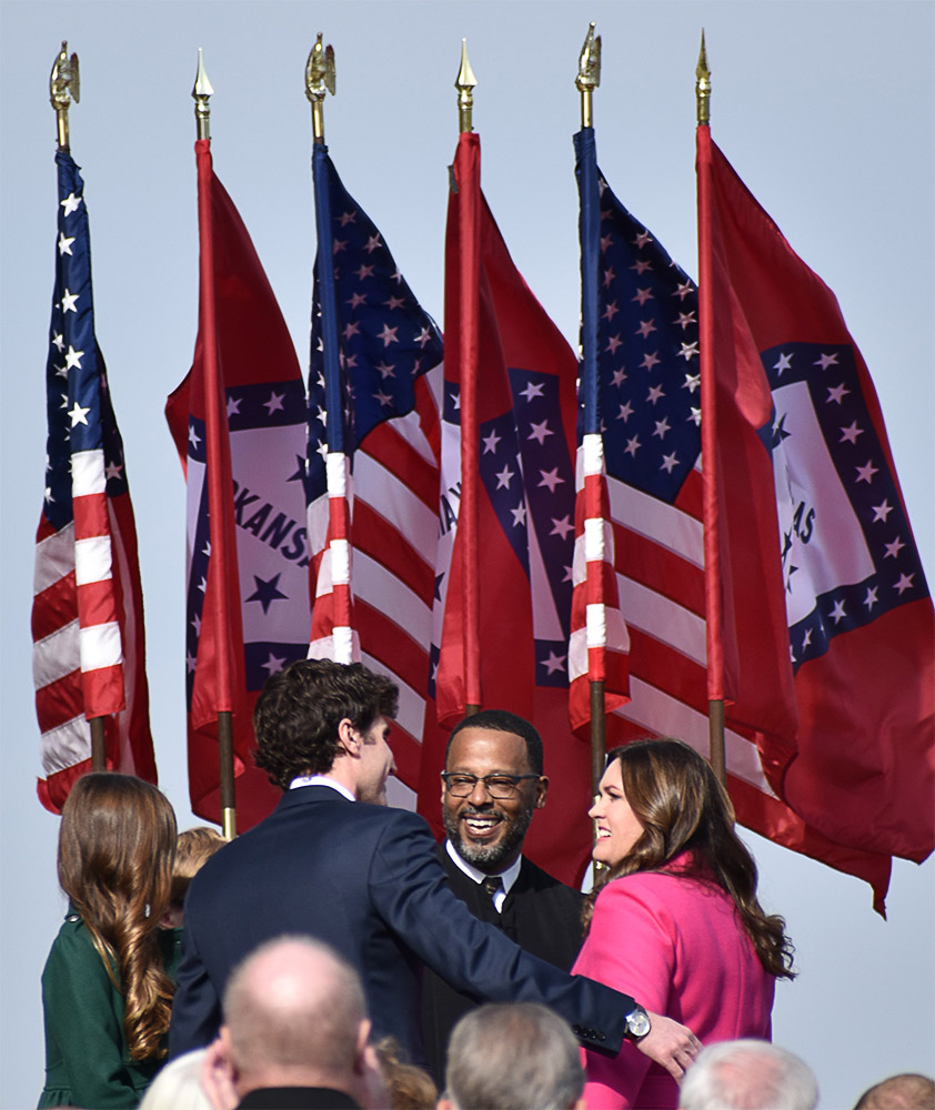 white woman in a hot-pink suit standing next to a white man in a suit and a black man in judge's robes