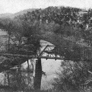 Metal bridge spanning river with trees and brush on river banks