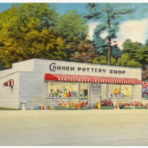 Postcard showing one story building with red and white striped awning and flowers in front and colorful pottery inside
