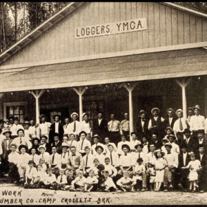 Large group of white adults and children in front of wooden building with sign saying "Loggers YMCA"