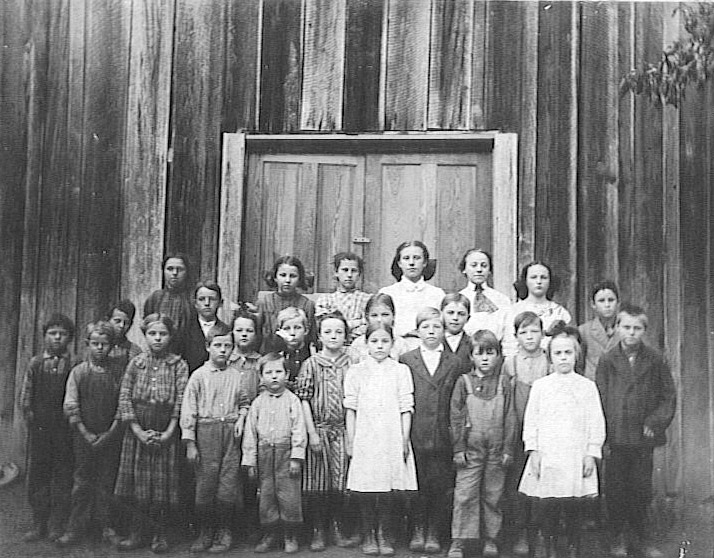 Group of school children gathered in front of wooden building