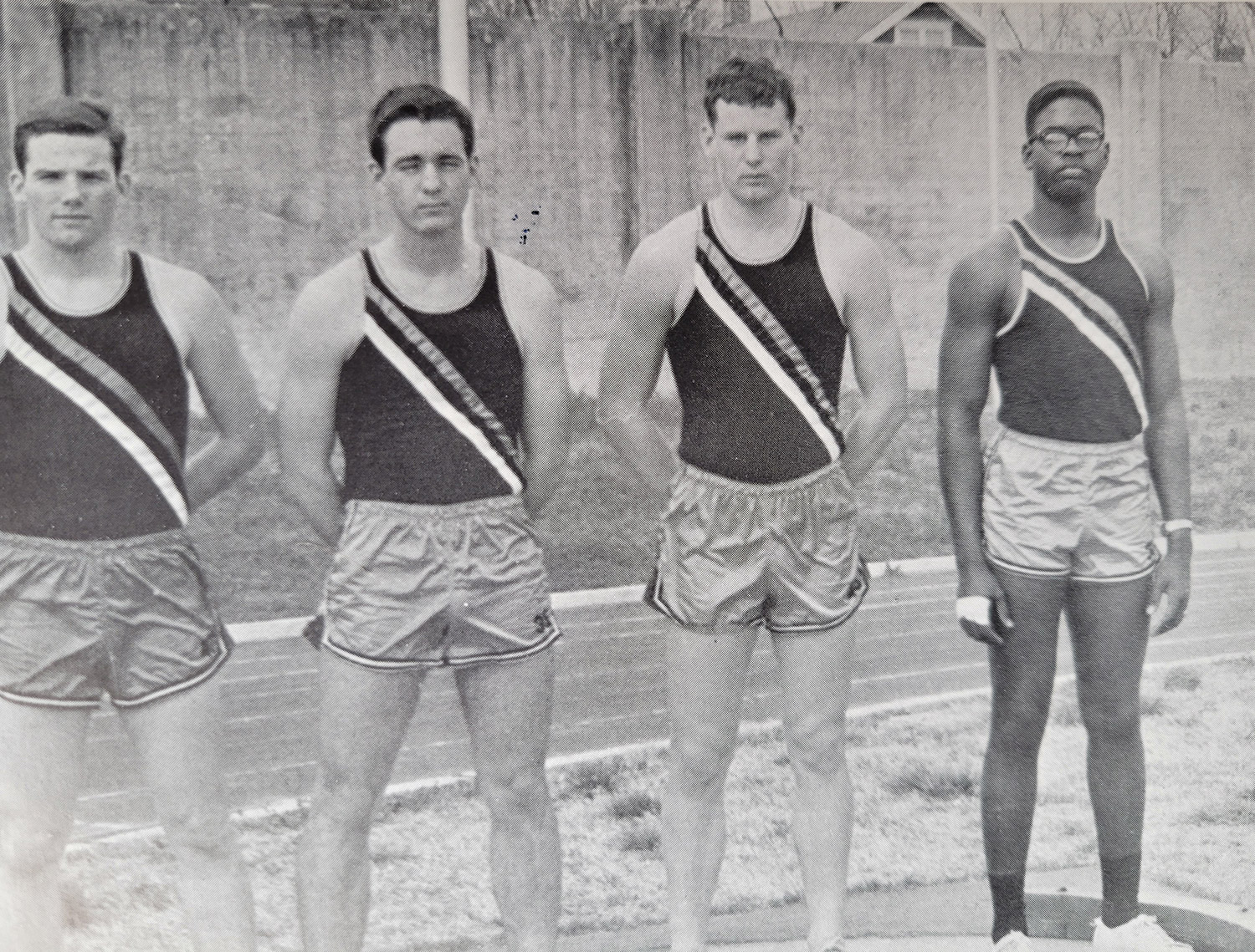 Three white young men and one African American young man in track uniforms