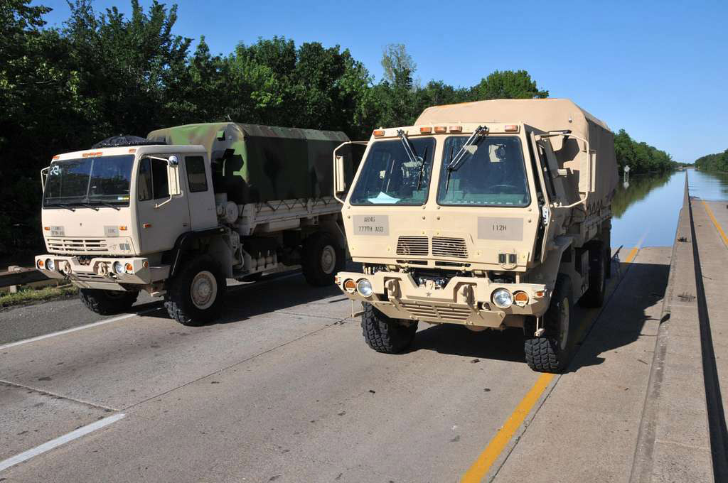 Two military vehicles parked on road near flooded section