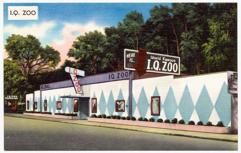 Postcard showing one story building with a blue diamond design and a sign saying "I.Q. Zoo"