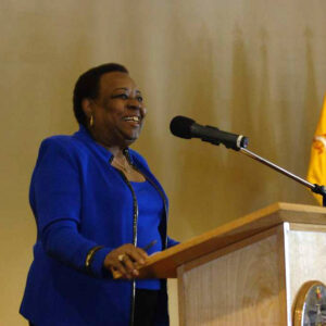 African American woman in blue outfit speaking into microphone at lectern