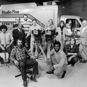 Large group of men and women standing before van with the words "Studio Five" on the side