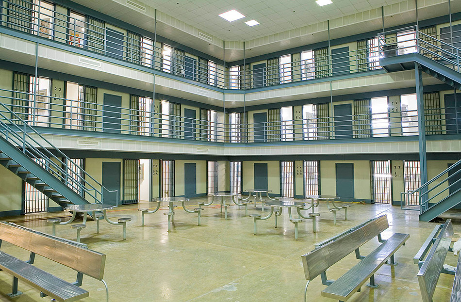 Interior of a prison showing three floors of cells and a center area with metal tables and benches