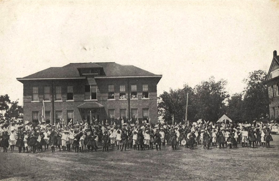 Large group of people gathered in front of multistory brick building