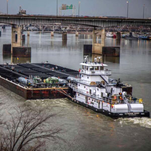 Tugboat pushing barges beneath bridges on river