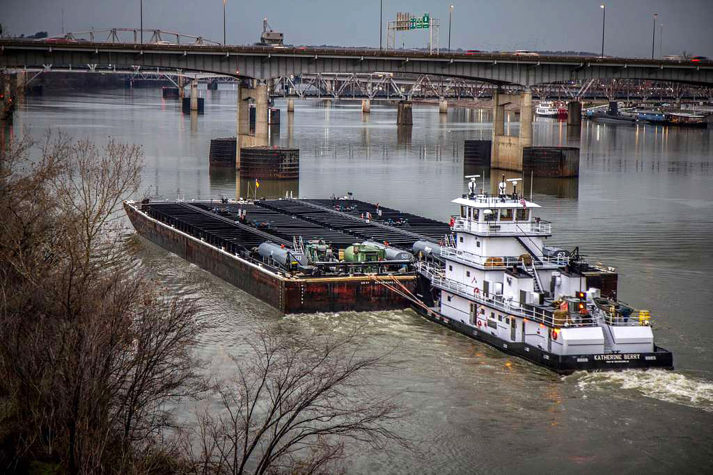 Tugboat pushing barges beneath bridges on river