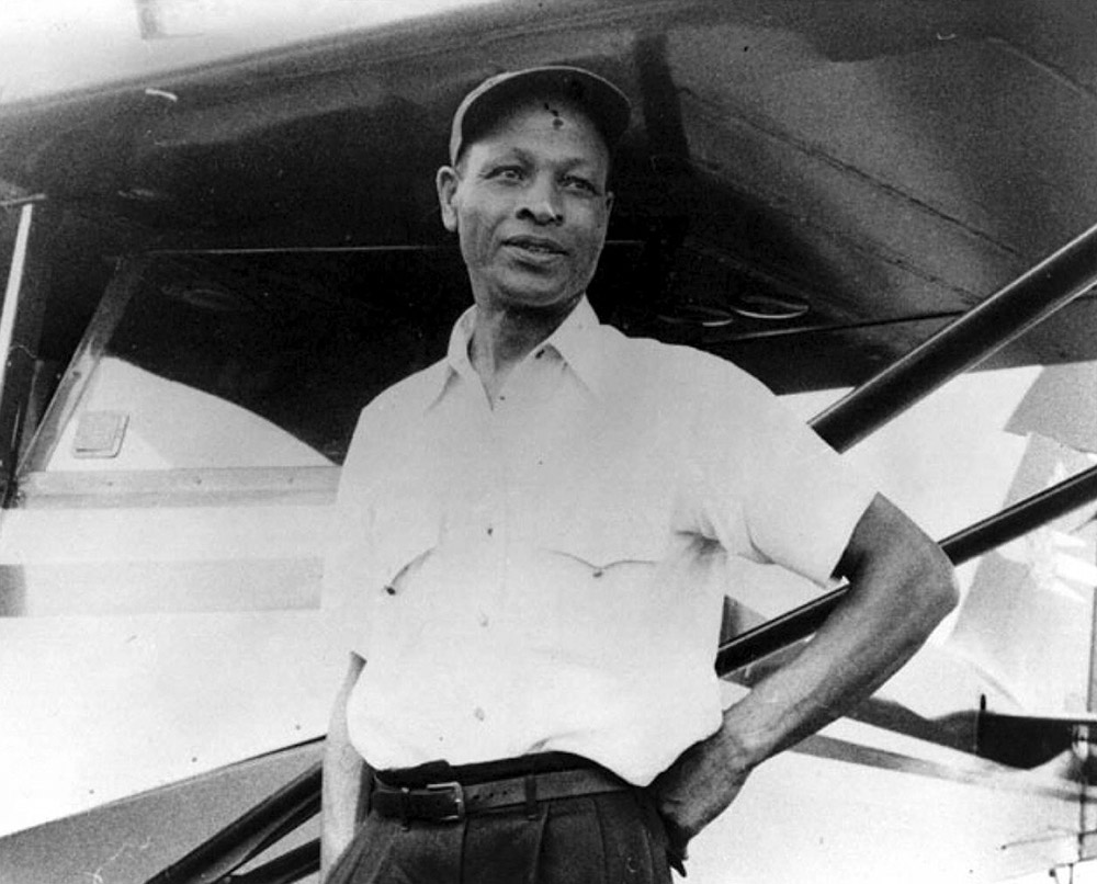 African American man in cap standing next to airplane