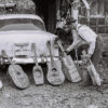 White man leaning interesting looking guitars against a car