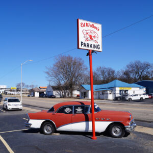 vintage red and white car parked in lot with window decal saying "only curb service beer in Arkansas"