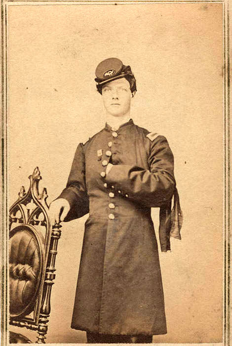 White man posing in formal military garb with hand resting on chair