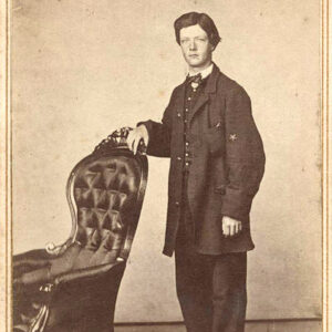 White man in ill-fitting baggy suit standing by chair