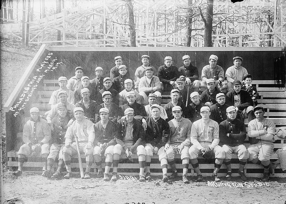 White men in baseball uniforms sitting on bleachers