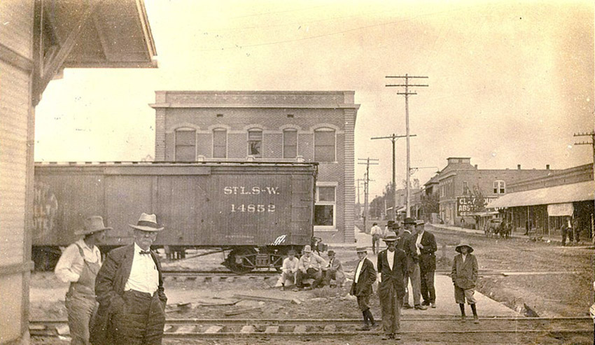 people standing near train tracks with rail car and town buildings in background
