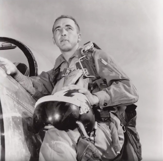White man in military pilot's garb climbing into the cockpit