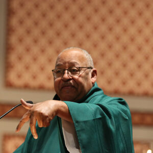 African American man in green priest's robes at microphone