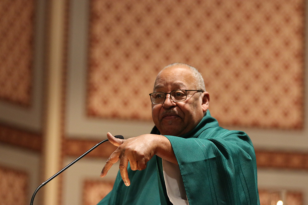 African American man in green priest's robes at microphone