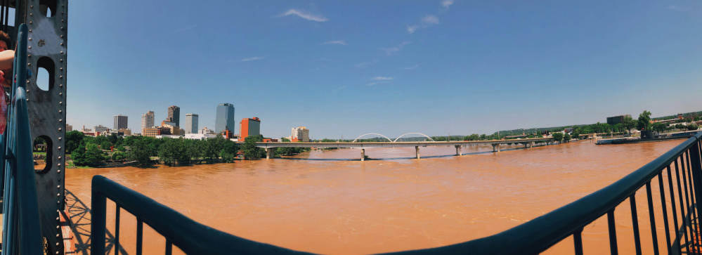 Flooded brown river between two bridges; city in background