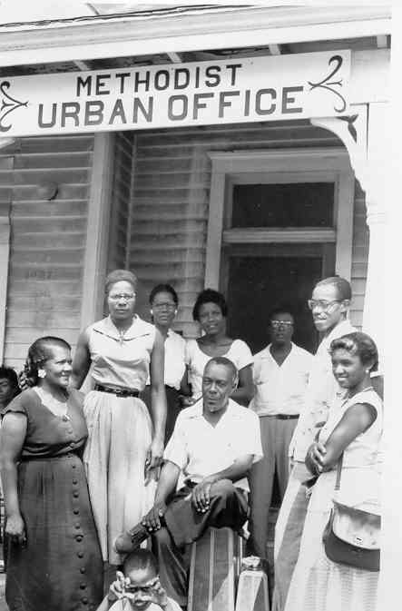 African American men and women and one child in front of building with sign saying "Methodist Urban Office"
