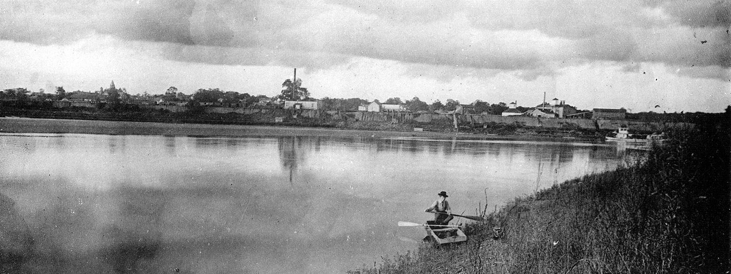 White child on river bank with small boat and oars with city seen in the distance