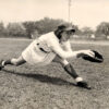 Woman in baseball uniform keeping foot on base as she stretches forward while holding baseball in glove