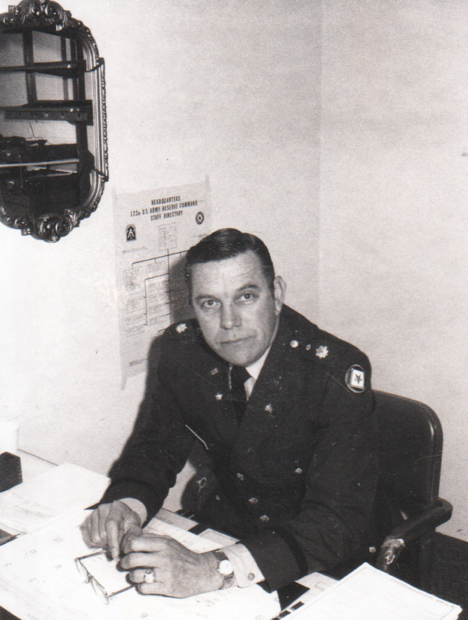White man in military garb sitting at desk
