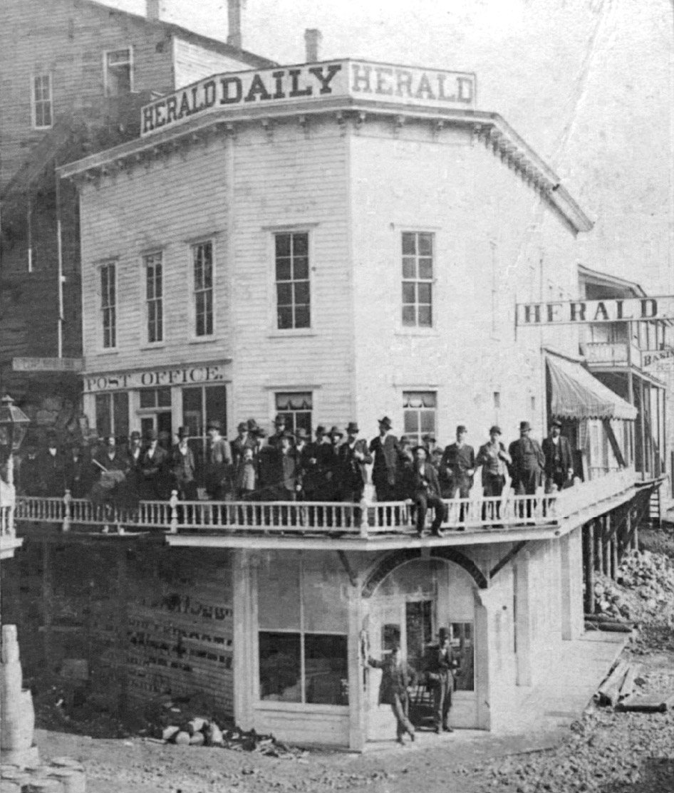 Large crowd of white men milling about by second floor exterior walkway of three-story building