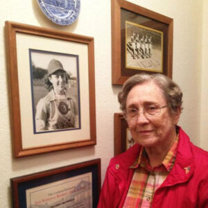 White woman dressed in red standing beside framed photos on wall