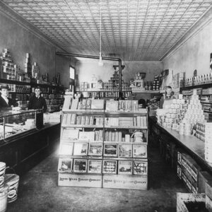 White men standing behind counters inside store with stacks of products