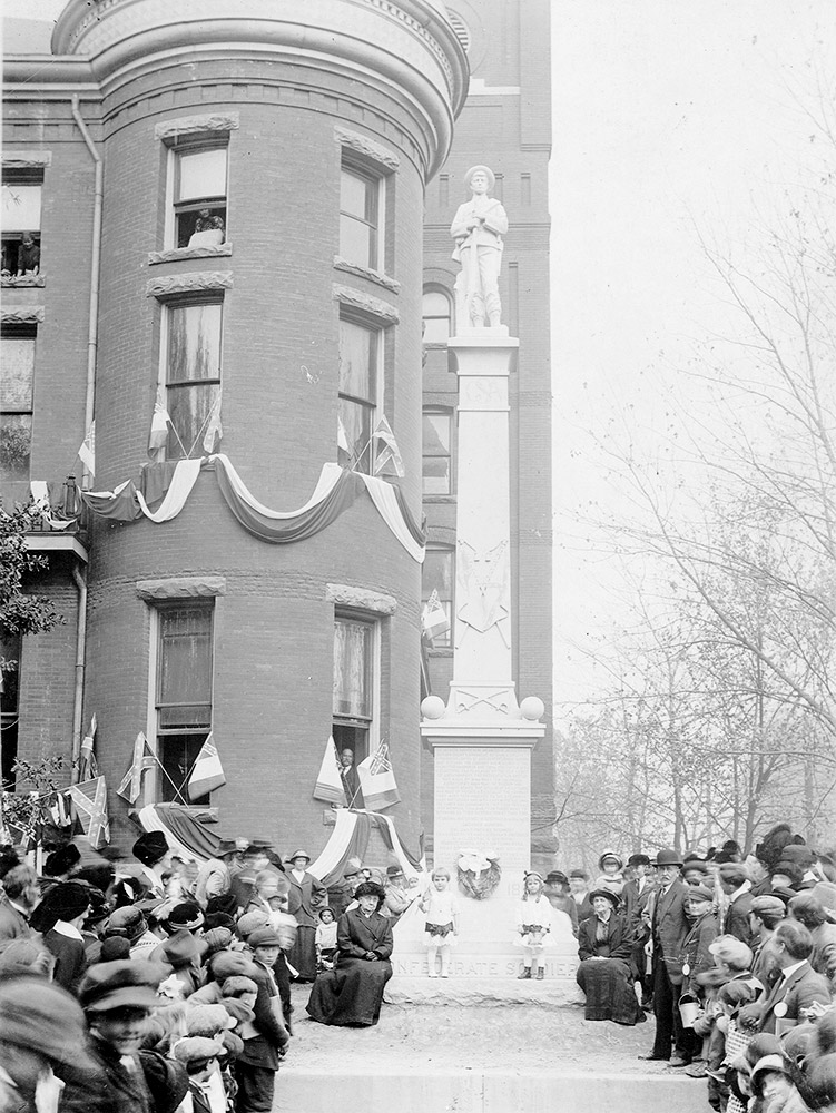 Large number of people gathered around a statue of a soldier