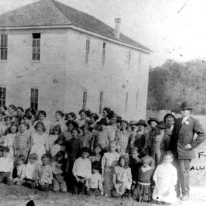 Large group of white children and adults in front of multistory white wooden building