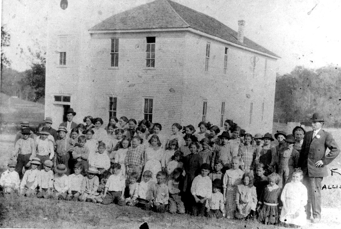 Large group of white children and adults in front of multistory white wooden building