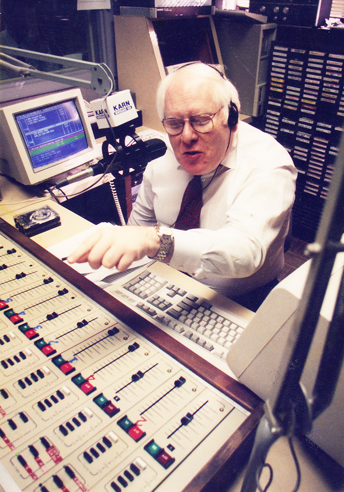 White man with glasses sitting at radio control panel