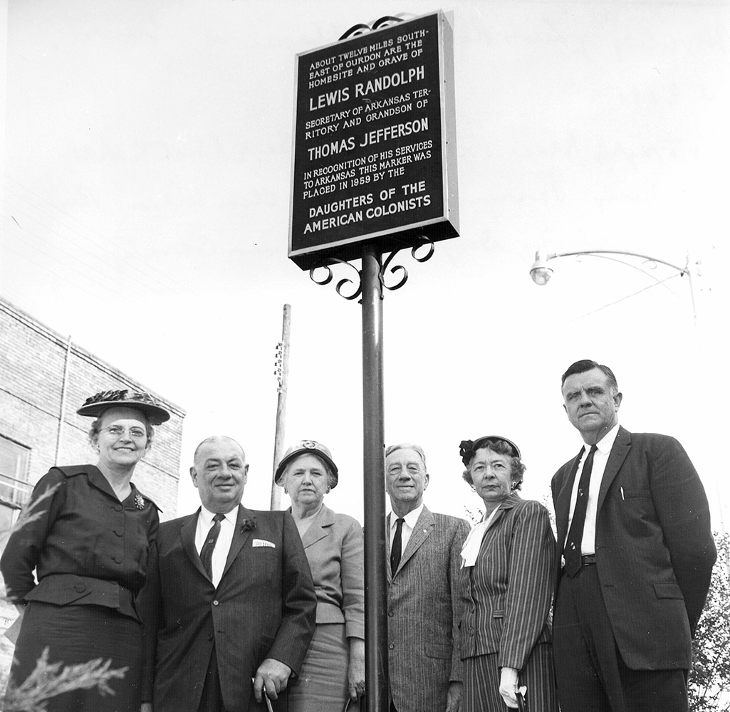 White men and women dressed in business attire standing beneath plaque