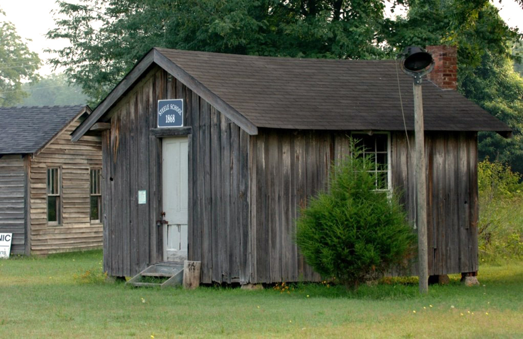 Single story wooden building with sign saying "Steele School 1868"