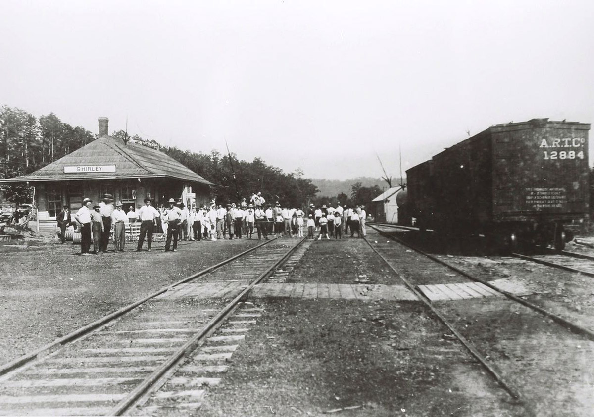 Large group of people standing beside train on railroad tracks