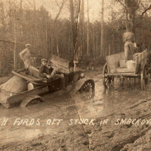Car stuck in mud being towed by team of horses; writing on photo says "even fords get stuck in smackover oilfield roads"