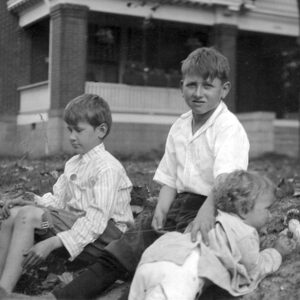 Three white male children on ground with large home in background