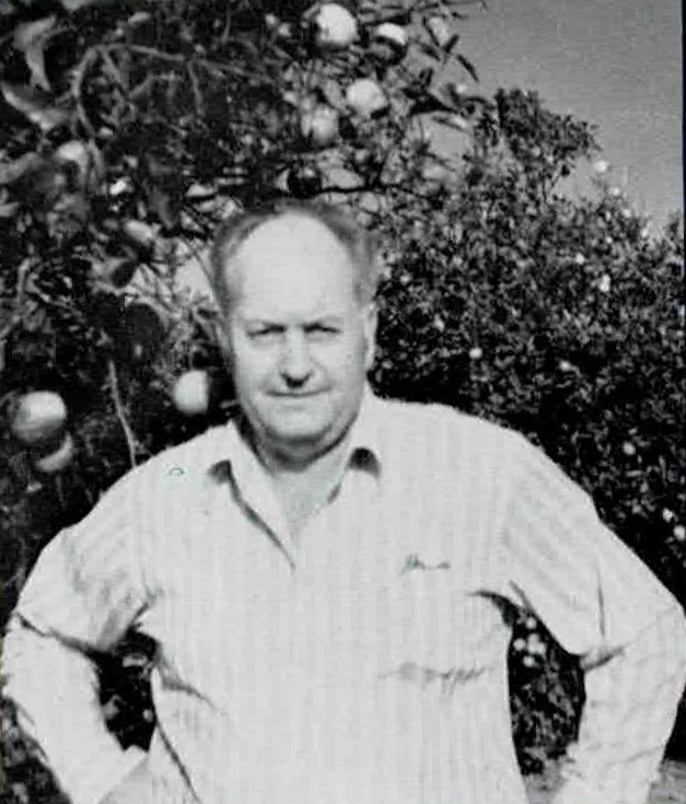 White man in light-colored striped shirt in front of fruit trees