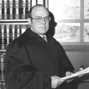 White man in suit and tie and glasses and judge's robe