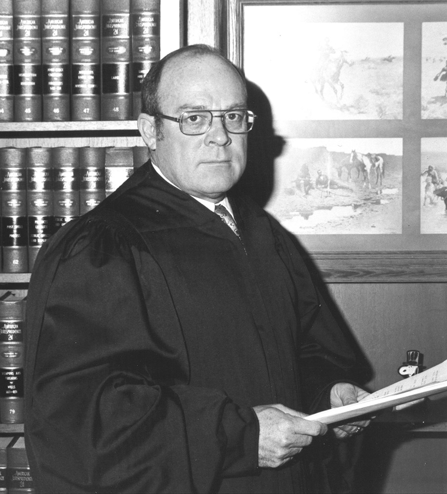 White man in suit and tie and glasses and judge's robe