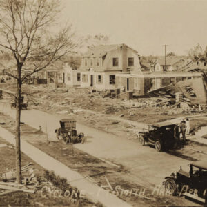 Cars driving down the street between rows of destroyed houses